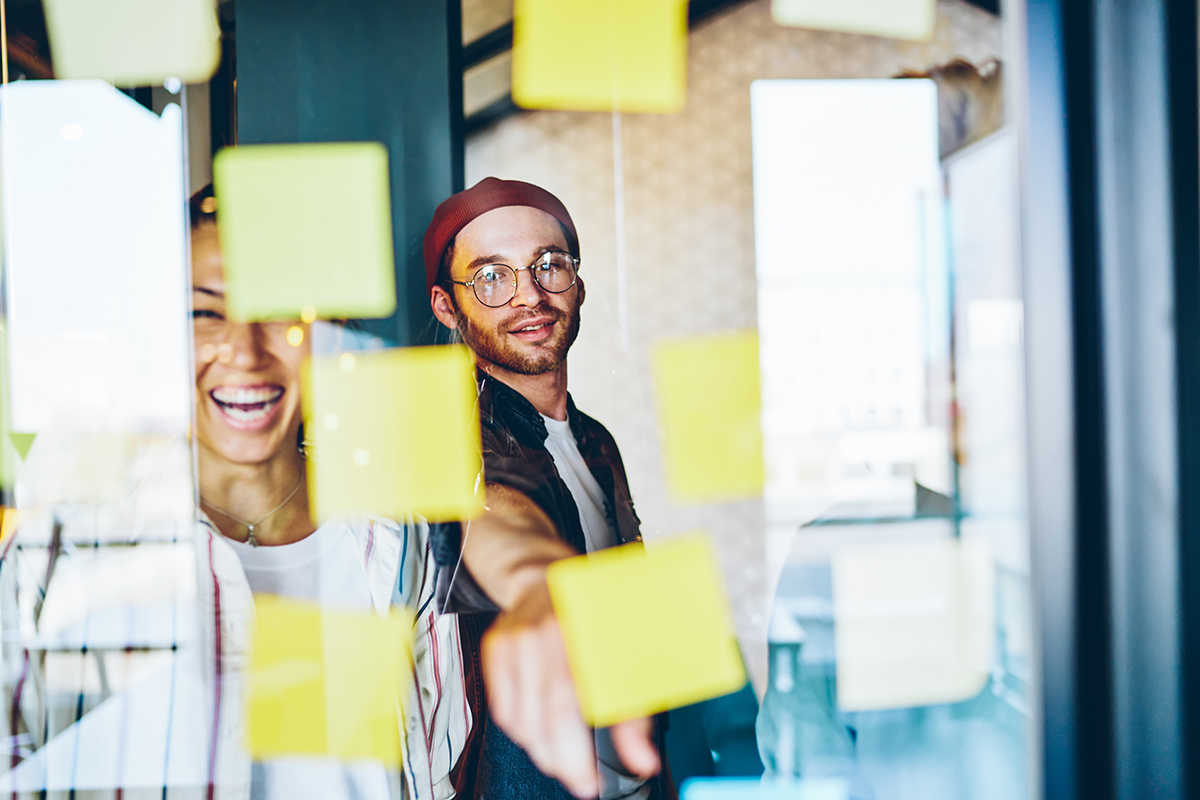 Cheerful,Caucasian,Male,Pointing,On,Sticker,With,Ideas,Having,Brainstorming Cheerful caucasian male pointing on sticker with ideas having brainstorming session with diverse group of employees, smiling asian girl satisfied with creative working process and team collaboration