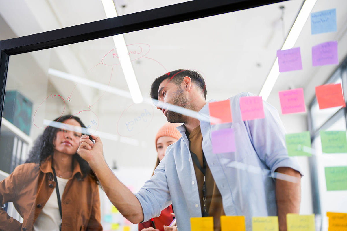 Dynamic,Brainstorming,Session,With,A,Focused,Team,Using,A,Transparent Dynamic brainstorming session with a focused team using a transparent idea board to strategize in the office.